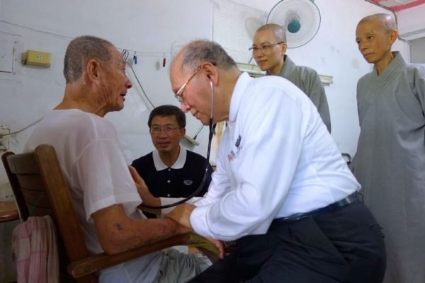 靜思精舍兩位法師(後排右一、二)、中區人醫會醫師紀邦杰(前排右一)，前往林弘展(左後二)老家進行居家往診與關懷，紀邦杰為林父(左前一)看診。